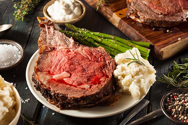 Prime rib cooked beautifully on a white plate, resting on a wooden dining table.